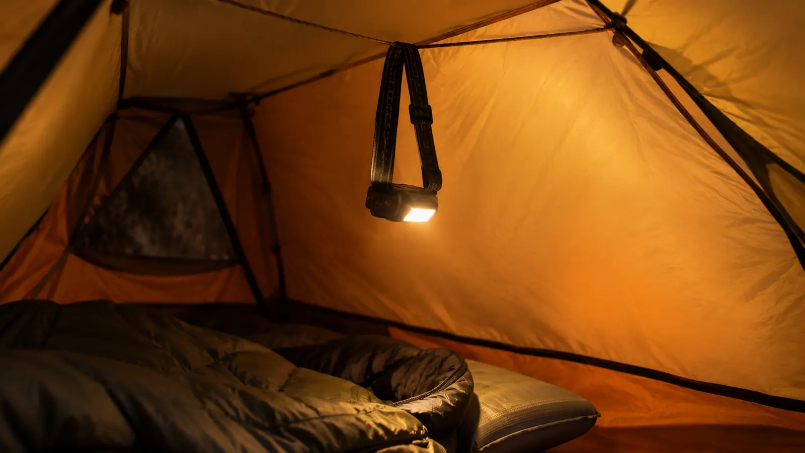 A headlamp hanging from a ridgeline inside a tent, lighting the interior